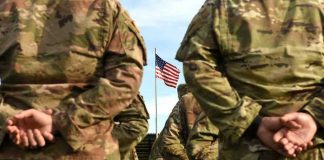 Soldiers stand in formation with American flag in background