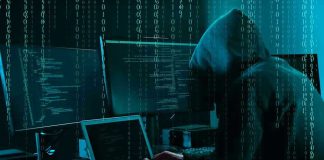 Hacker in dark room surrounded by computer screens