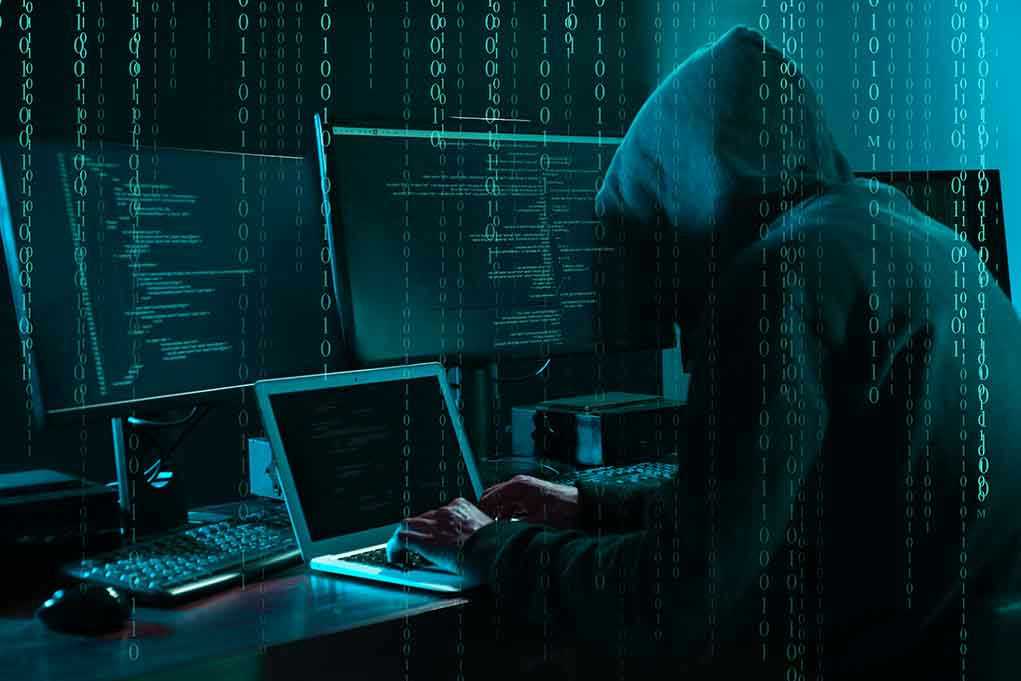 Hacker in dark room surrounded by computer screens