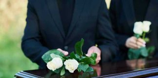 People placing white roses on a casket