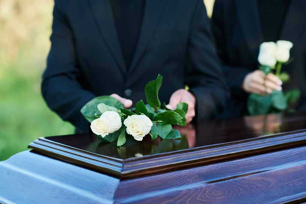 People placing white roses on a casket