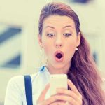 Surprised woman looking at her smartphone outdoors