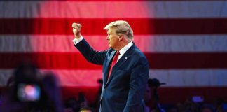 Person in suit with fist raised in front of flag