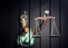 Blindfolded Lady Justice statue holding scales behind bars