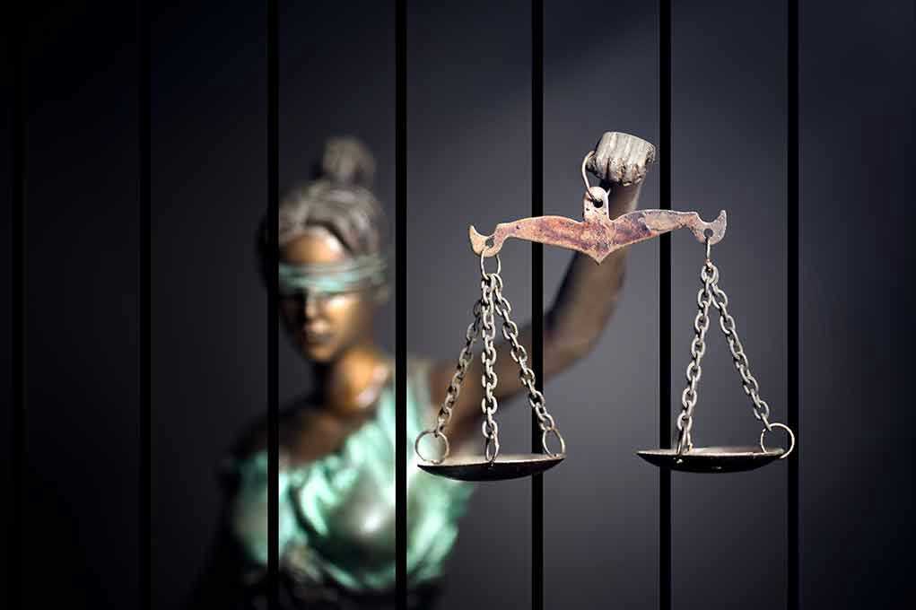 Blindfolded Lady Justice statue holding scales behind bars