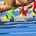 Athletes starting a sprint from starting blocks on a blue track