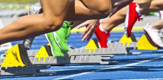 Athletes starting a sprint from starting blocks on a blue track
