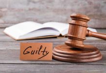 A wooden gavel next to a card that reads guilty and an open book