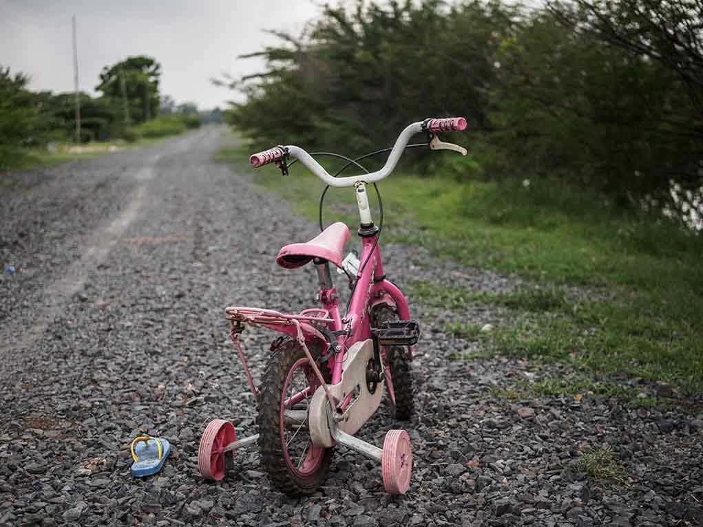 Pink childrens bike with training wheels on gravel path.