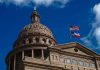 Building dome with US and Texas flags blue sky