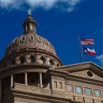 Building dome with US and Texas flags blue sky