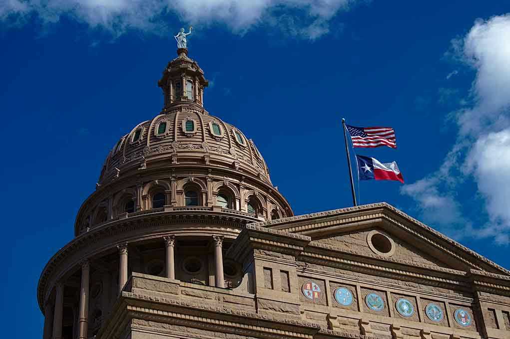 Building dome with US and Texas flags blue sky