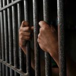 Trusted Aide Turns Predator—Family Catches Horror on Tape Hands gripping prison cell bars tightly.