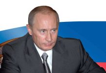 Putin Orders Nuclear Test Prep — Alarm Bells Ring A serious looking man in a suit sitting at a table with a Russian flag in the background