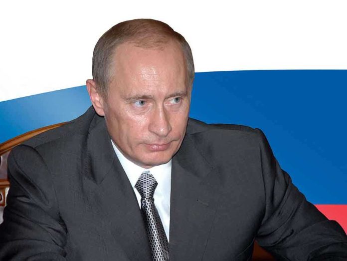 A serious looking man in a suit sitting at a table with a Russian flag in the background