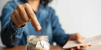 Person placing a coin into a savings jar labeled 'SAVINGS'