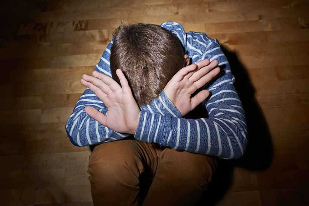 A child sitting on the floor with their hands covering their face, expressing distress