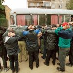 Group of men with hands on their heads near a bus during a police operation