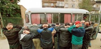Group of men with hands on their heads near a bus during a police operation