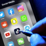 Netflix Director’s $11M Ferrari Scandal Social media apps on phone screen with hand holding stylus.