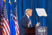 Trump FIRES Protected Bureaucrat — Supreme Court SHOWDOWN Person speaking at podium with flags in background.