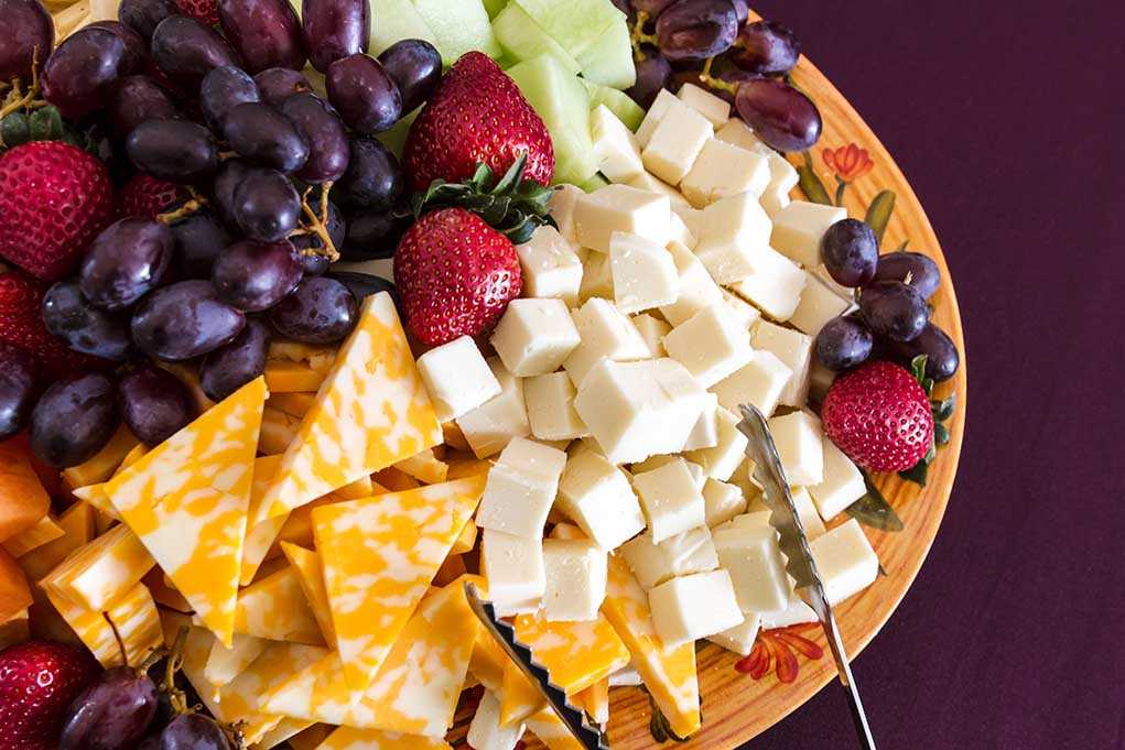 A colorful cheese and fruit platter featuring various cheeses and fresh fruits