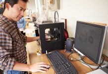 A person working at a desk with a 3D printer and computer