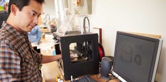 A person working at a desk with a 3D printer and computer