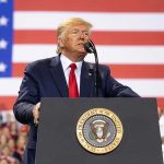 Trump’s Insurrection Threat Shakes Minnesota Man speaks at podium with U.S. flag background.