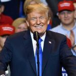 Trump SHUTS DOWN Kennedy Center — Two YEARS! Man in suit speaking at rally with red hats.