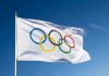 Olympic flag waving against clear blue sky.