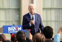 Man speaking at an outdoor event with Biden sign.