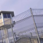 Shocking Surge: Immigration Detention Suicides EXPOSED Guard tower behind barbed wire fence in a prison.