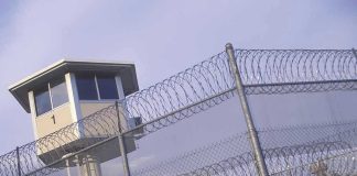Shocking Surge: Immigration Detention Suicides EXPOSED Guard tower behind barbed wire fence in a prison.