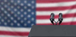 Podium with microphones in front of American flag.