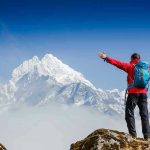 CLOSE CALL: Glacier National Park Shock Hiker with arms outstretched in front of snowy mountains.