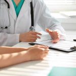Hidden Truth: PCOS Mislabeling Affects 170 Million Doctor discussing with patient, holding clipboard on desk.