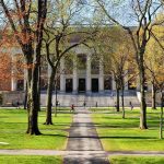 Campus Chaos Unleashed — Parents Be Warned! Students walking on a university campus with autumn trees and a historic building in the background