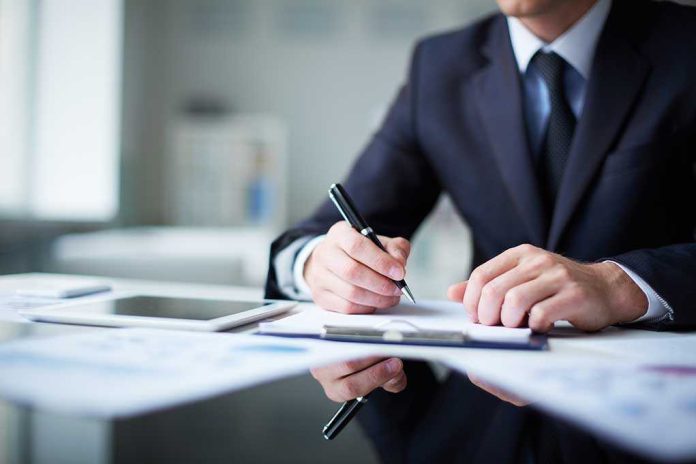 shutterstock_160448204 A man in a suit writing notes at a desk with documents and a tablet