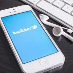 Smartphone displaying the Twitter logo next to keys and earphones on a desk