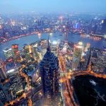 Weak April Data Sparks China Anxiety! Aerial view of Shanghais skyline at night with illuminated buildings and a river