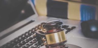 A wooden gavel resting on a desk with a laptop in the background