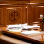 ChatGPT Tied To Killings, State Explodes Wooden courtroom desk with papers and a microphone.
