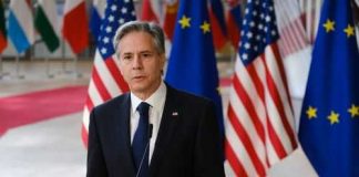Man in suit speaking at podium with international flags behind