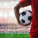 Soccer player holding a ball in a stadium with a cheering crowd