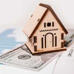 Wooden house model on money and contract papers