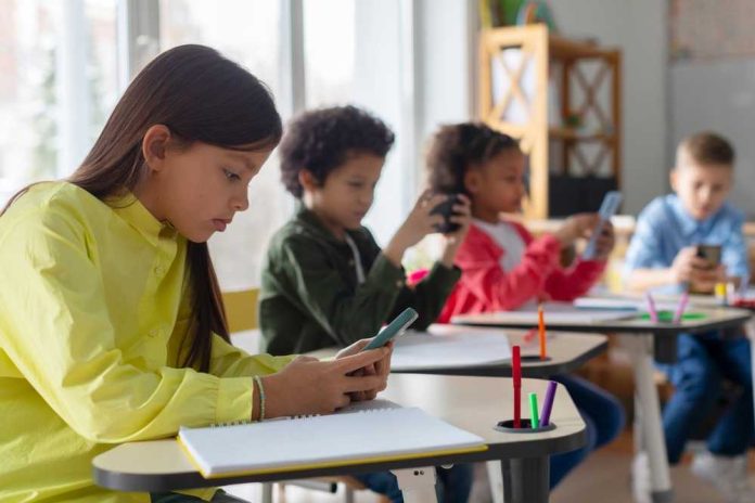 shutterstock_2471109447 Students using smartphones at classroom desks
