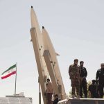 soldiers stand beside large missiles at outdoor display