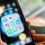 Hands holding a smartphone showing social media app icons