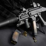 Silencer Registry Stumbles—What’s Left? Submachine gun with suppressor and magazines on dark surface